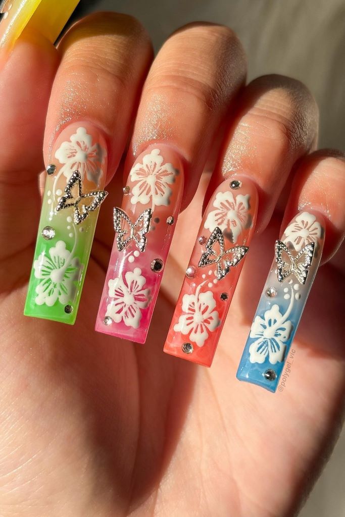 Trendige Nagelkunst mit Ombre-Effekt, Blumen und glitzernden Schmetterlingen.